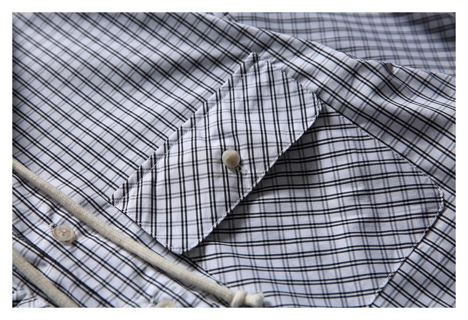 Close-up of a pointed collar and button on the light shirt with a black plaid pattern.