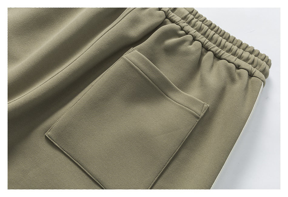 Close-up of a rectangular pocket on olive-gray pants beside the elastic waistband.