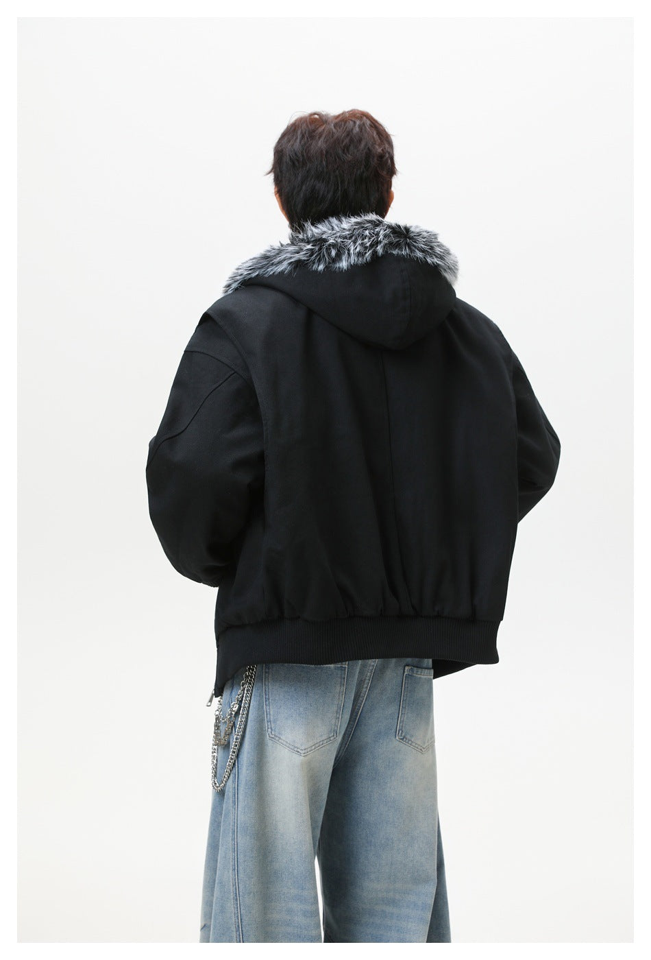 Rear view of a model wearing a black jacket with gray faux-fur trim around the hood.