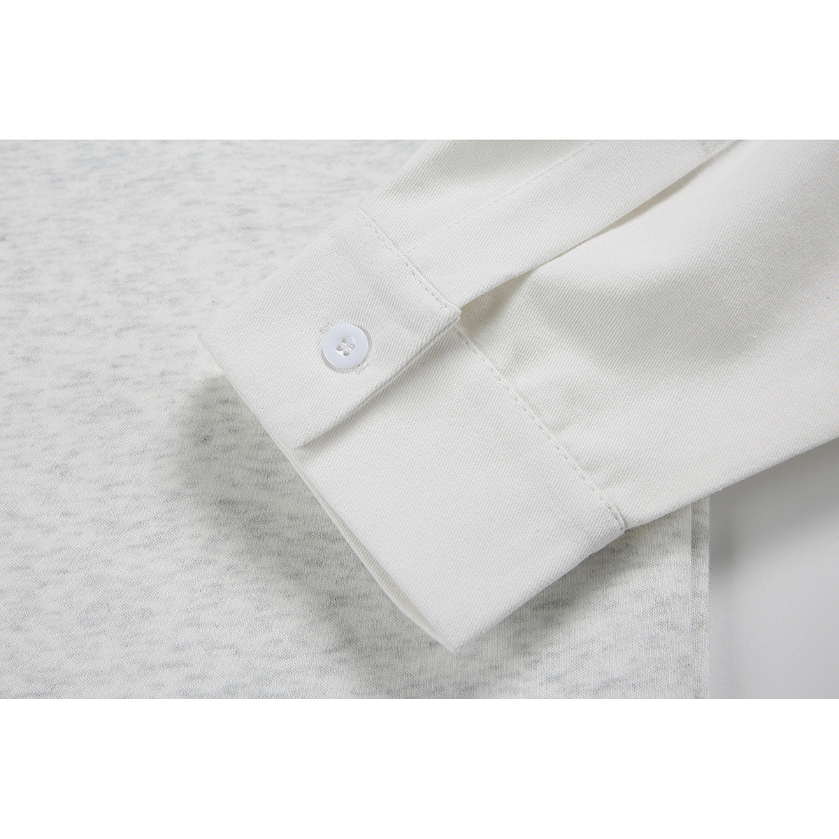 Close-up of a white buttoned cuff against light gray mottled shirt fabric.