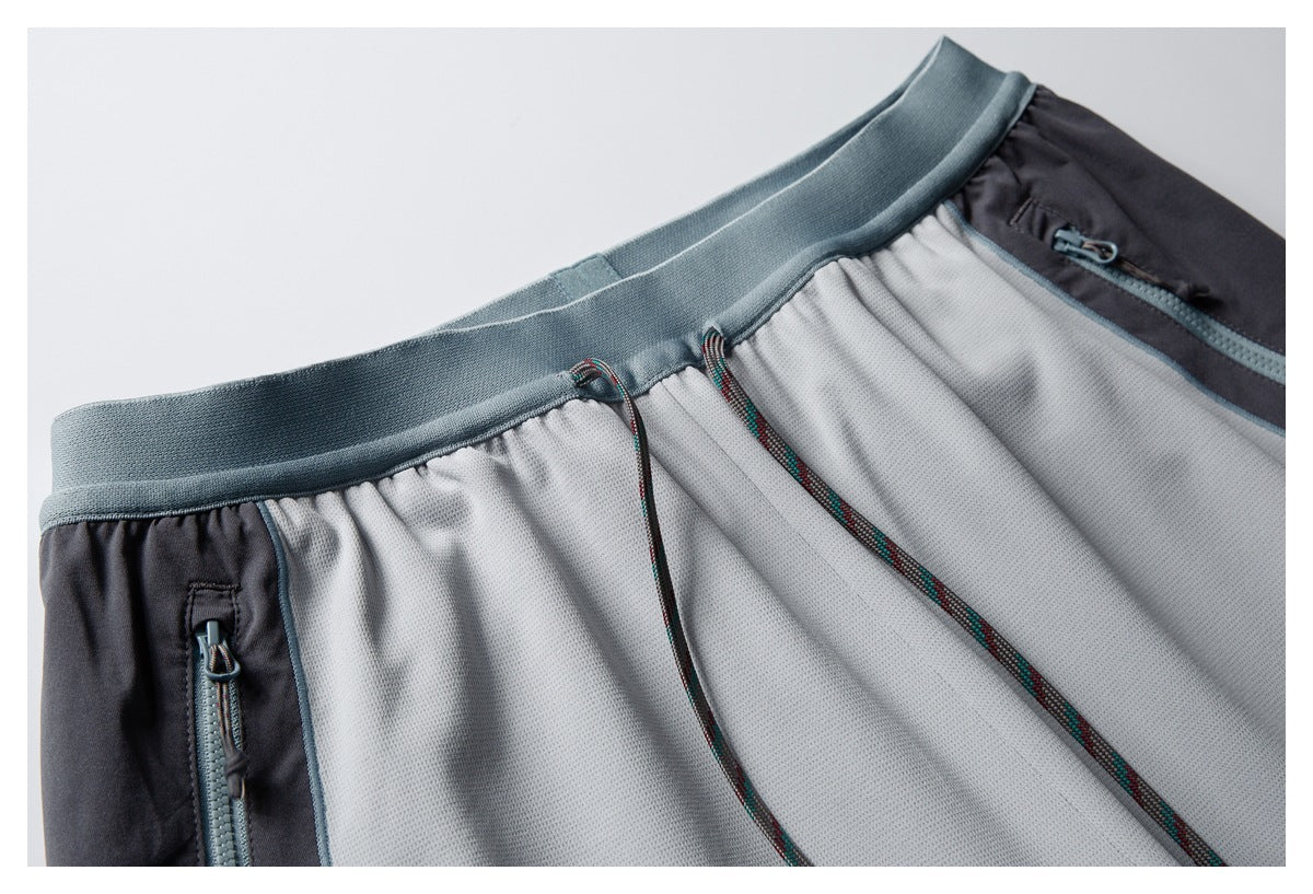Close-up of the pants' blue-gray waistband, patterned drawstrings, and zip pocket against a dark panel.
