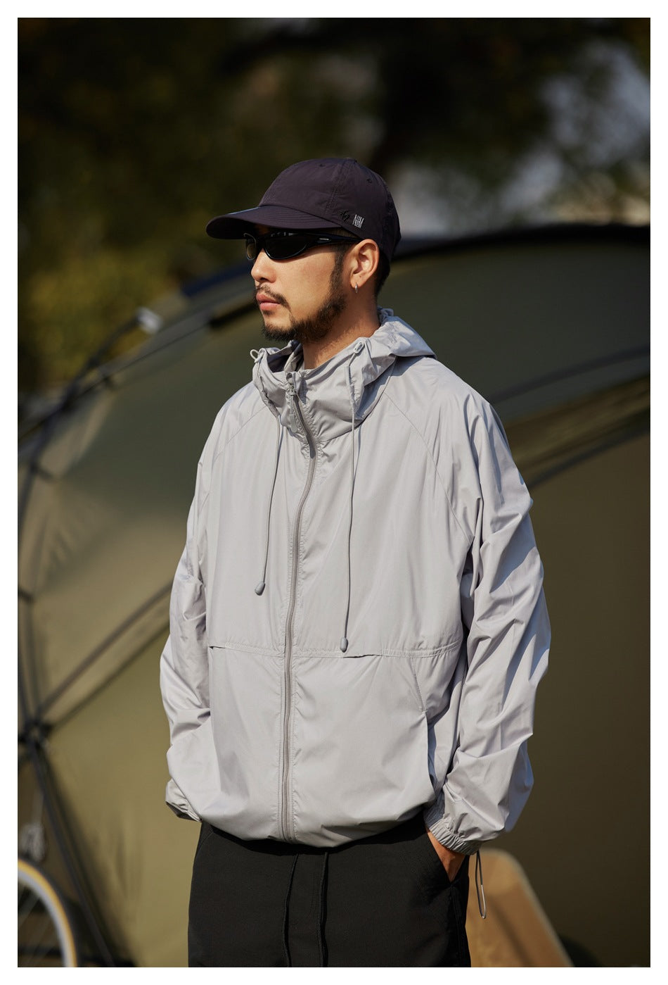 Man wearing a light gray hooded zip jacket with drawcords and elastic cuffs, paired with black pants.