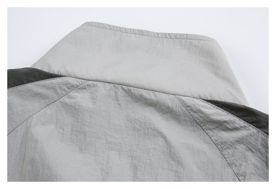 Close-up of a light gray jacket's raised collar and stitched upper-back panels, with dark gray sections at the sides.