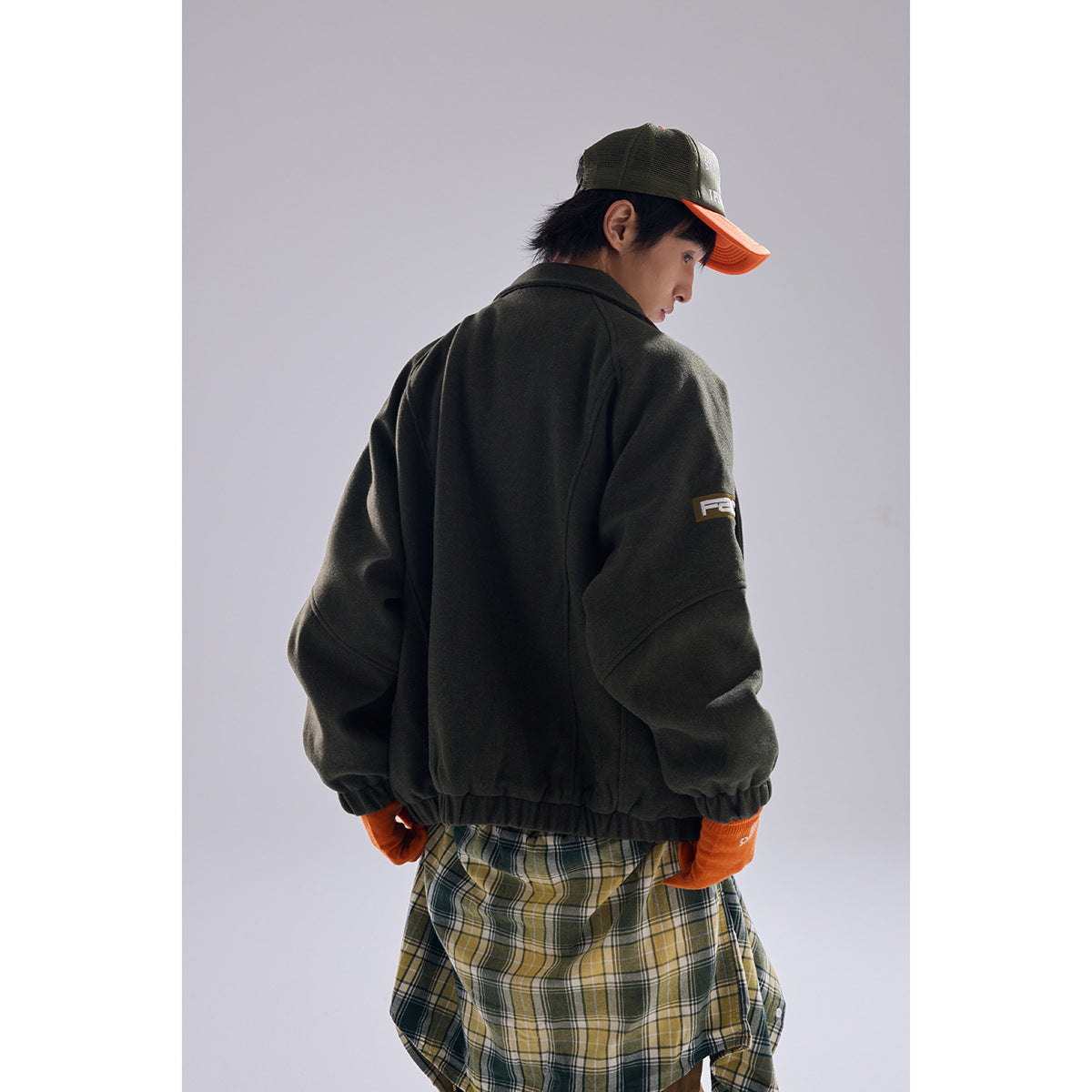 Rear view of a model wearing a dark olive jacket with a sleeve patch and elastic hem.