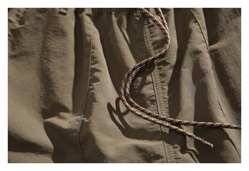 Close-up of taupe shorts fabric and a patterned drawcord crossing the front.