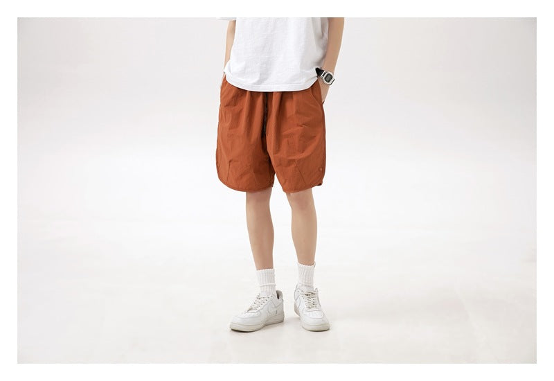 Cropped front view of rust-orange shorts with a dark drawstring waist, worn with a white T-shirt.