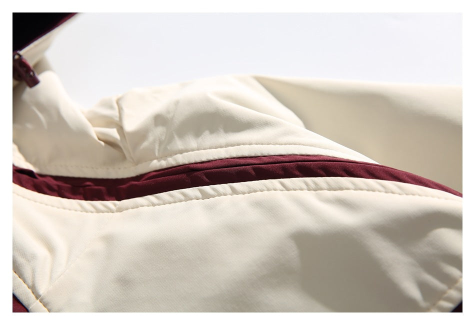 Close-up of cream jacket fabric with a curved burgundy color-block panel and stitched seams.