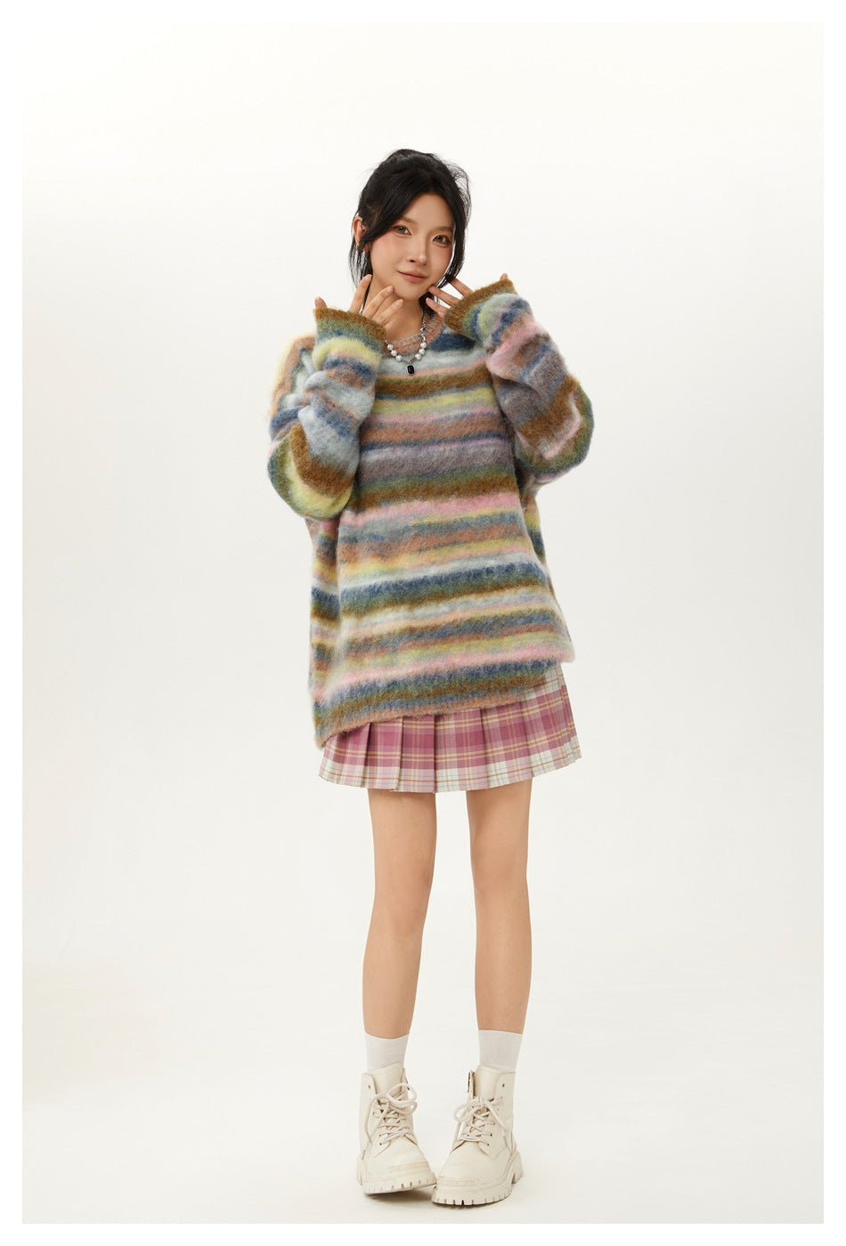 Full-length front view of a model in a multicolor striped oversized sweater, pink plaid skirt and white lace-up boots.