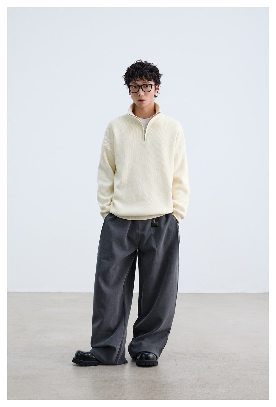 Full-length view of model in cream quarter-zip sweater, gray wide-leg trousers and black chunky shoes