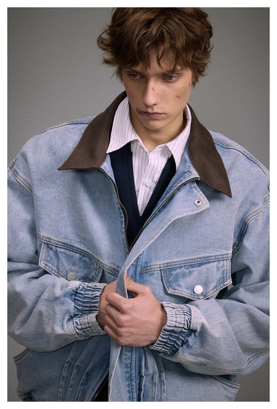 Close-up of a model showing the denim jacket's brown collar, buttoned flap pockets, zipper, and gathered cuffs.