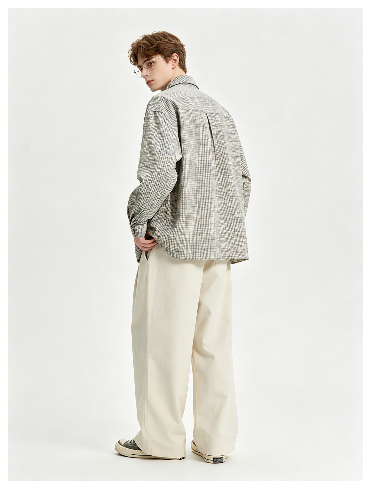 Model seen from the back in a gray check long-sleeve shirt with back yoke and center pleat, with cream wide-leg pants