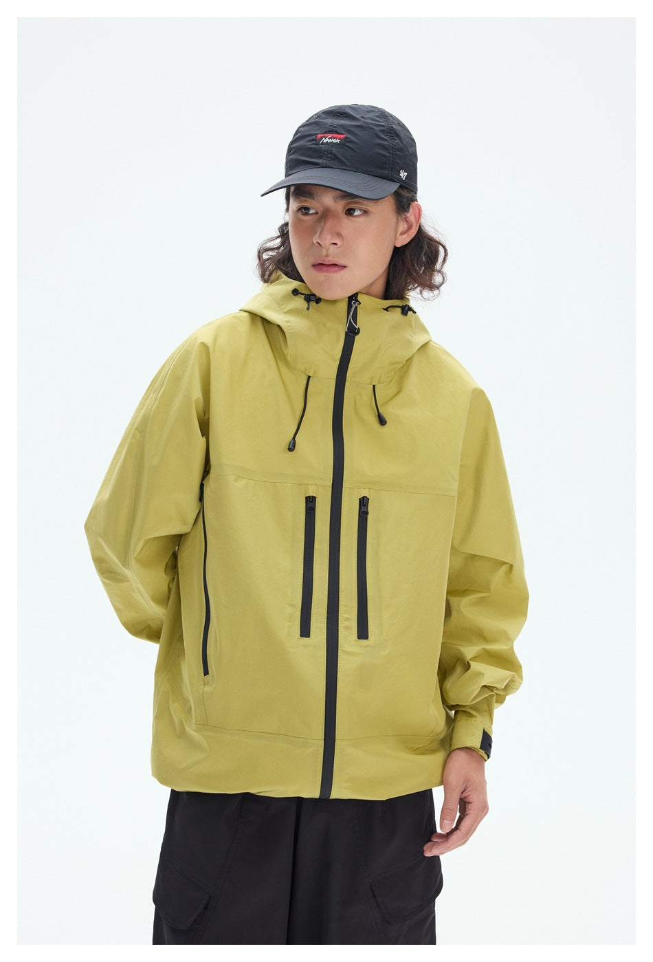 Model wearing a yellow hooded jacket with a full-length black zipper and several vertical zip pockets.