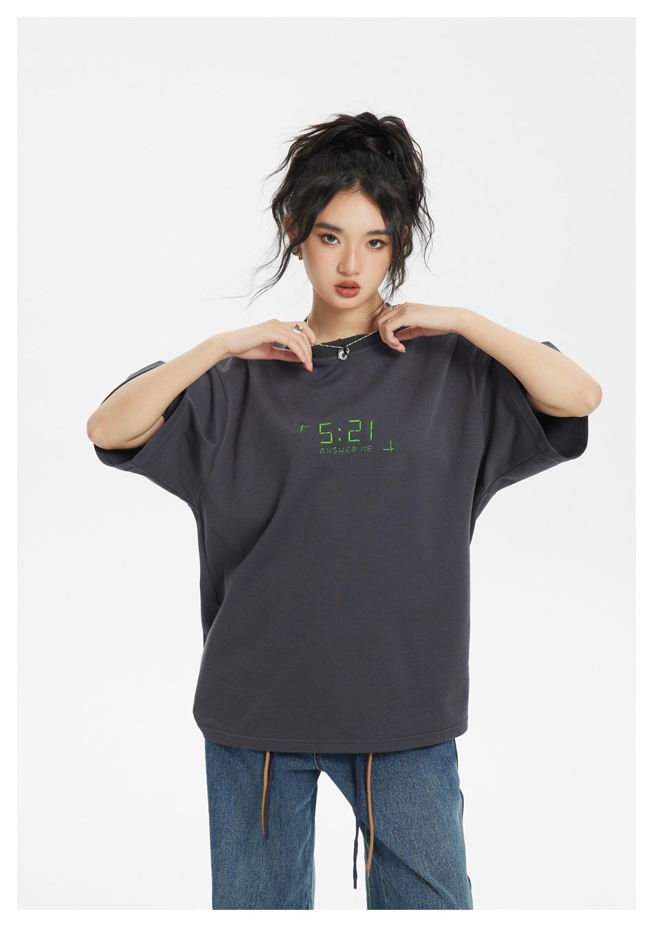 Model wearing a charcoal oversized T-shirt with green chest lettering, shown from the waist up.
