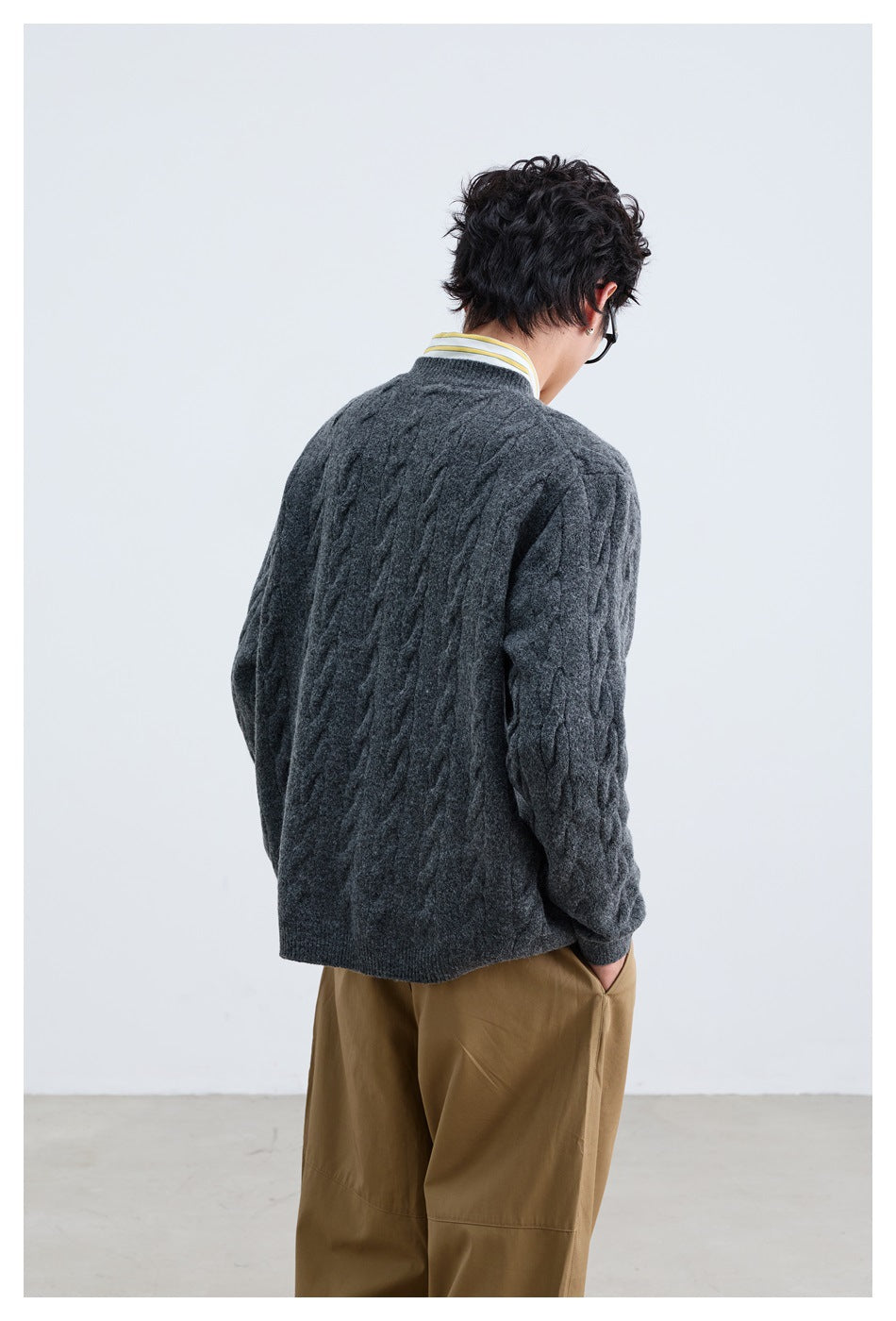 Back view of a model wearing a charcoal gray cable-knit cardigan with tan trousers.