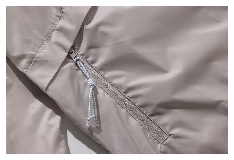 Close-up of a slanted zipper and white cord pull on a light taupe jacket.