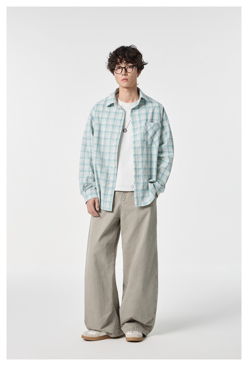 Full-length model wearing an open pale blue-and-white plaid shirt, white tee, and loose taupe trousers.