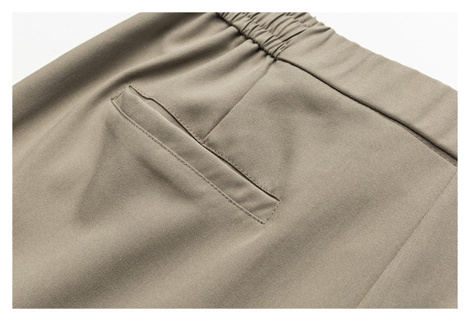 Close-up of a slim welt pocket and elasticated waistband on taupe trousers.