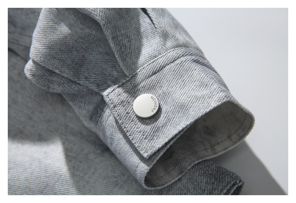 Close-up of a light gray denim jacket cuff with a round white button marked “FASHION.”