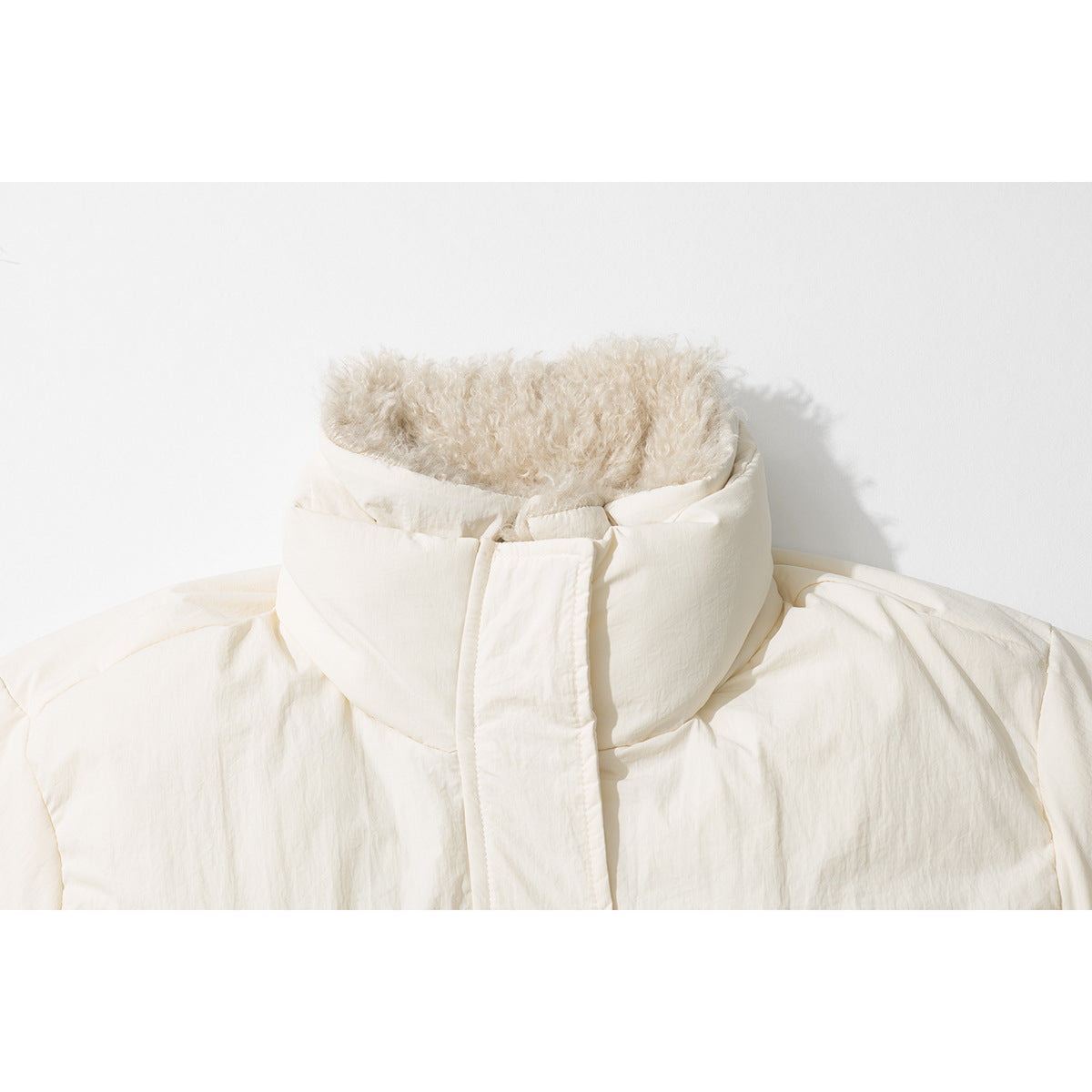 Close-up of a cream puffer jacket’s tall collar, showing its fluffy lining and covered front closure.