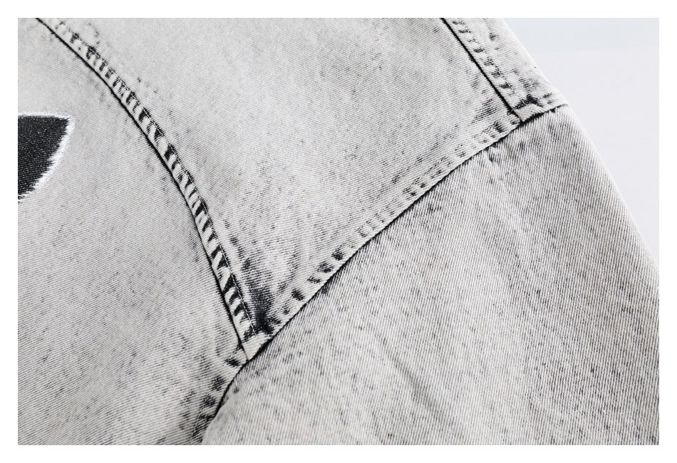 Close-up of light gray acid-wash denim with dark seam stitching and part of a black garment graphic.
