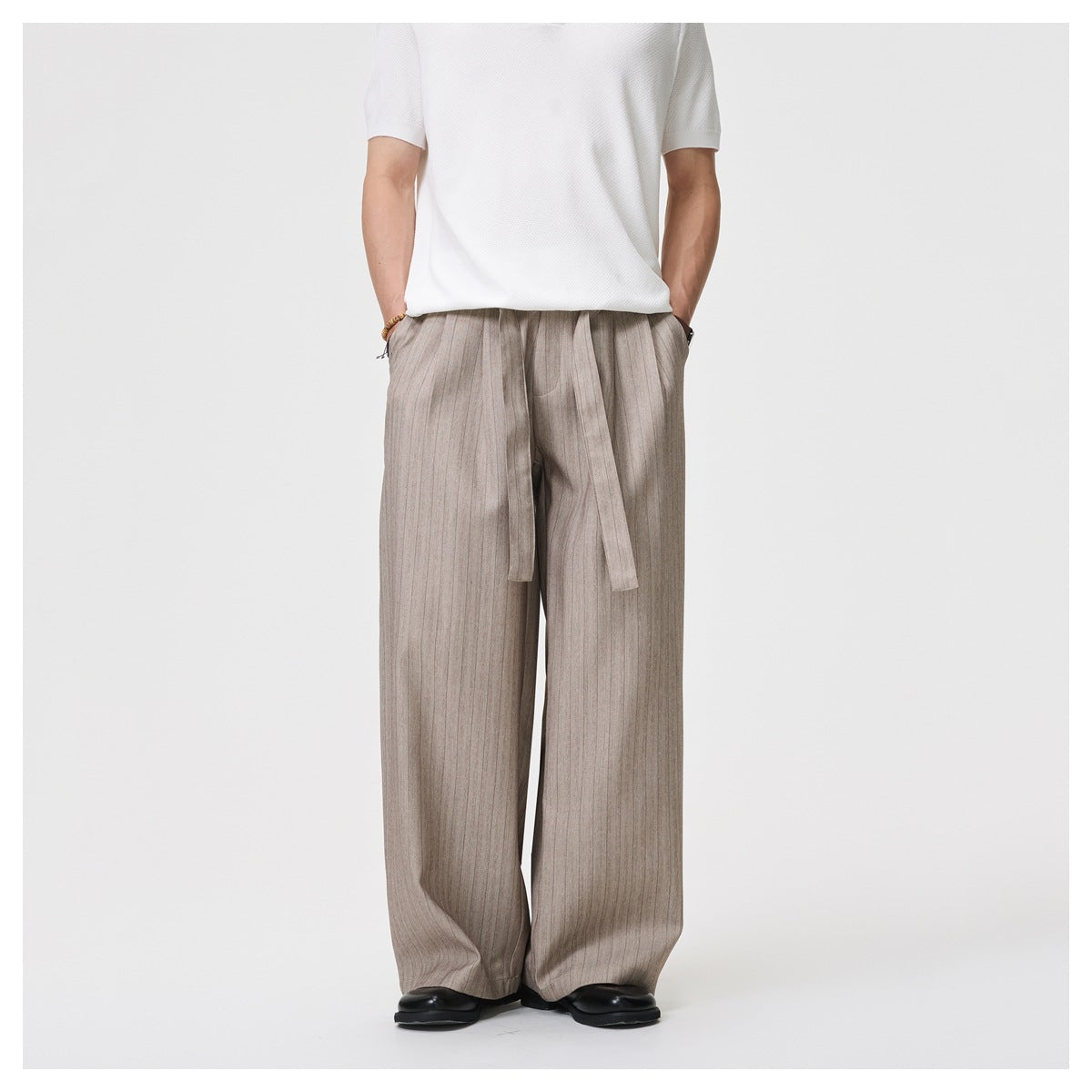 Front view of a model wearing loose taupe-gray pinstriped trousers with a long waist tie.
