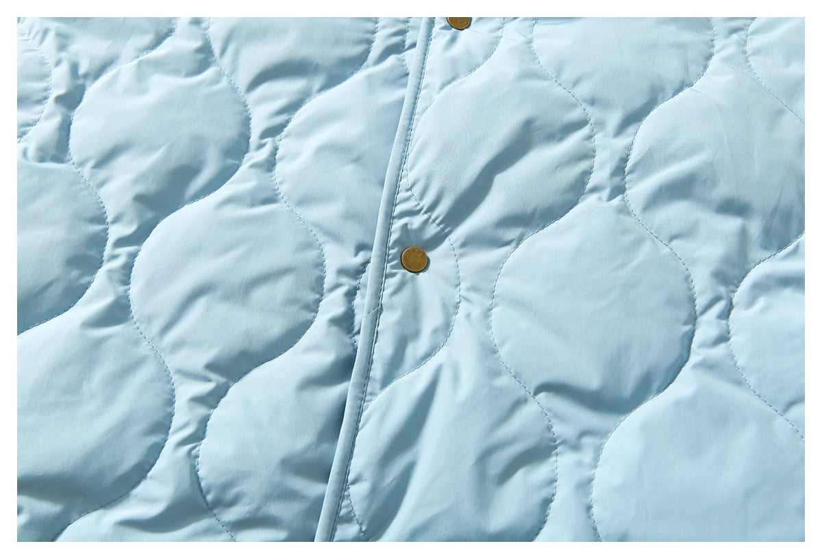 Close-up of the light blue jacket's rounded quilting and front placket with brass-tone snap buttons.
