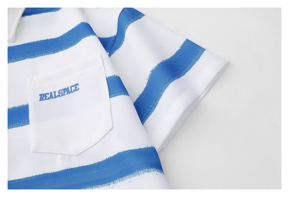Close-up of the white shirt's chest pocket and short sleeve, showing blue brushstroke stripes and embroidered lettering.