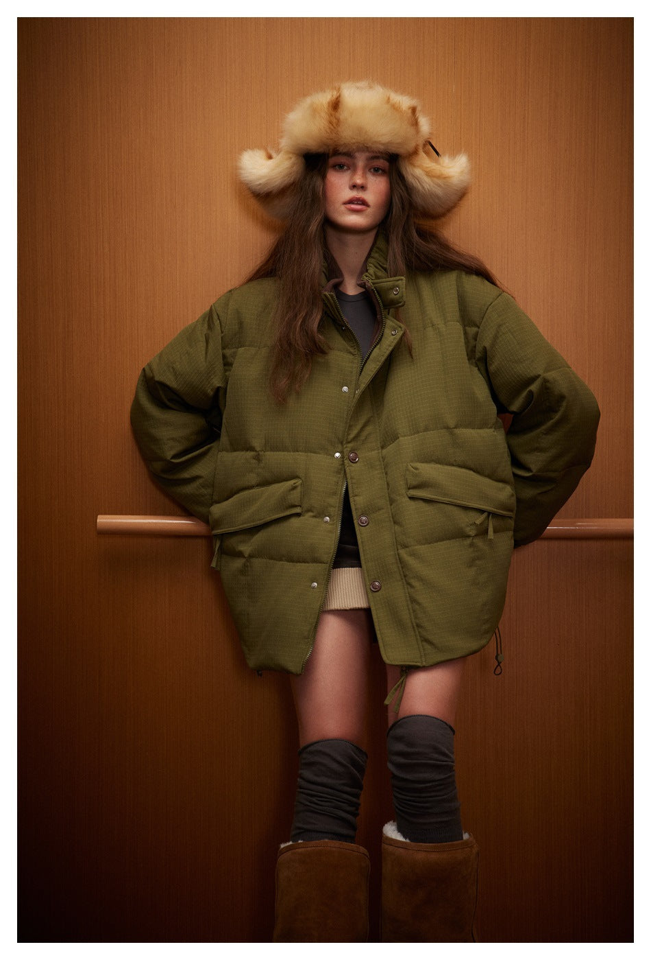 Front view of a model in an oversized olive quilted jacket with a high collar, snap closure and large flap pockets.