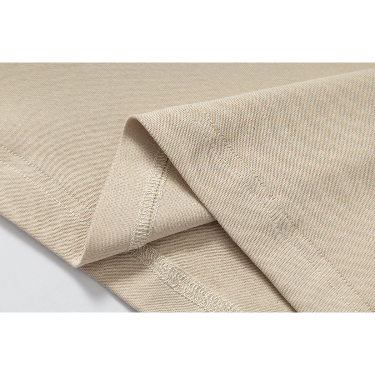Close-up of beige shirt fabric folded to show the stitched hem and overlocked seam.