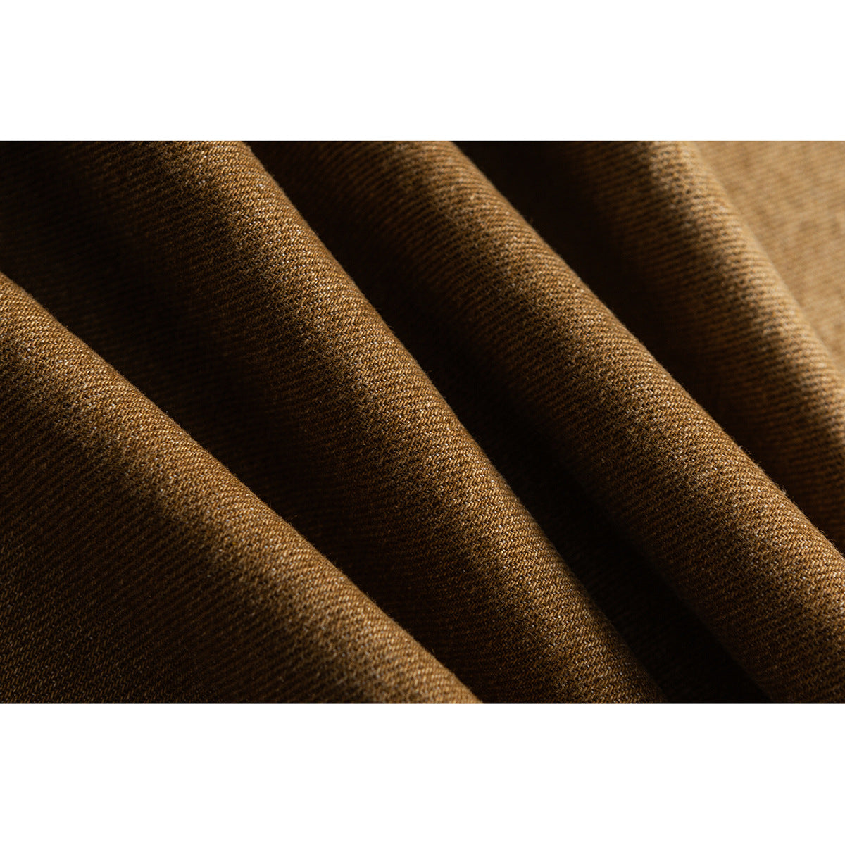 Macro view of brown woven fabric folded into soft ridges, showing its diagonal texture.