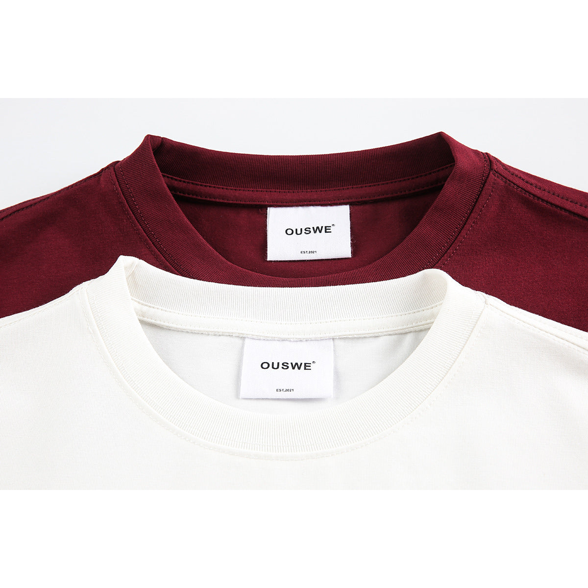 Close-up of cream and burgundy T-shirt crew necks with white OUSWE neck labels.