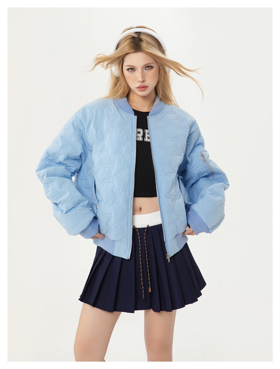 Model wearing a pale blue star-quilted bomber jacket over a black cropped top and navy pleated skirt.