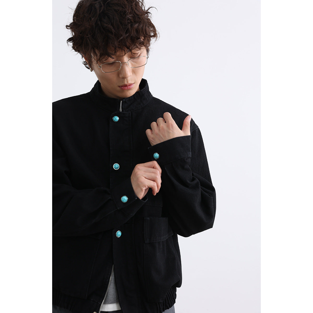 Close view of a model wearing a black jacket with turquoise buttons and wide cuffs.
