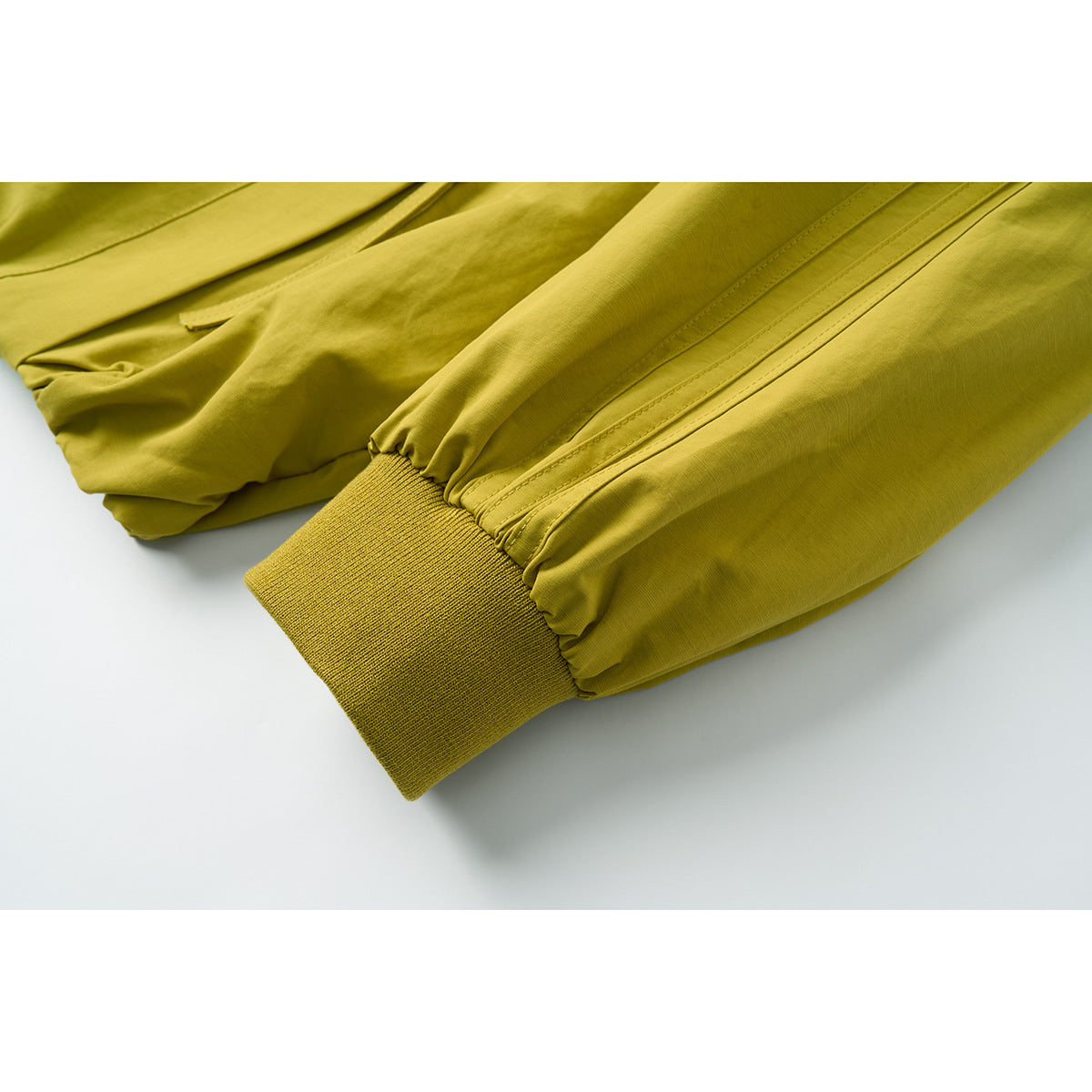 Close-up of a mustard yellow jacket sleeve with stitched panels and a ribbed cuff.