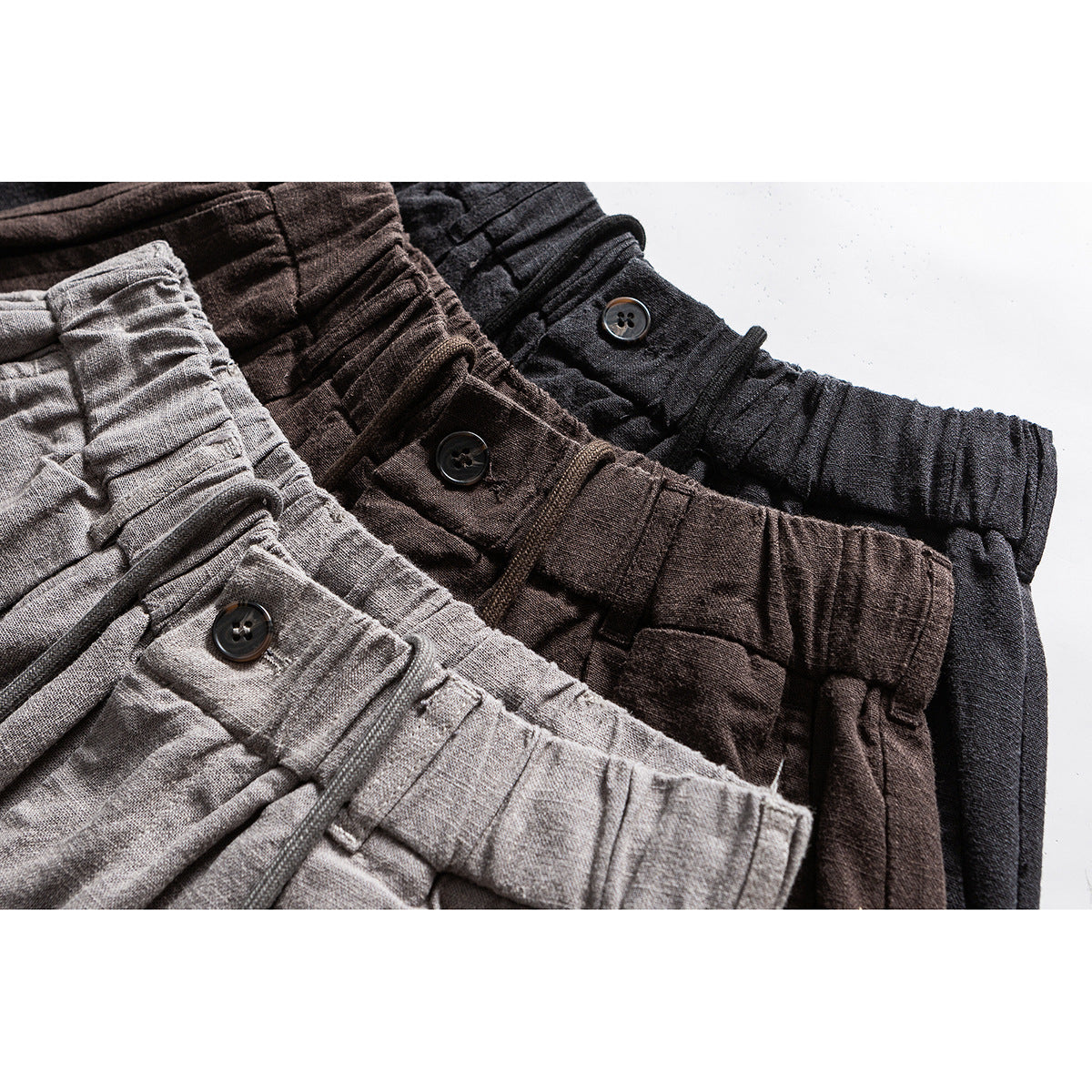 Close-up of gathered waistbands and dark buttons on light gray, brown, and black trousers.