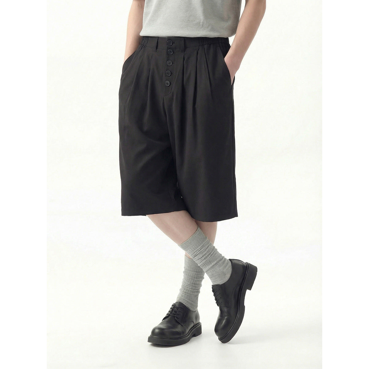 Cropped model wearing black pleated knee-length shorts with a button-front waist and side pockets.