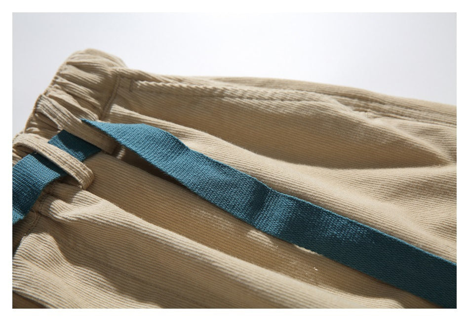 Close-up of a teal webbing belt threaded through loops on tan ribbed trousers.