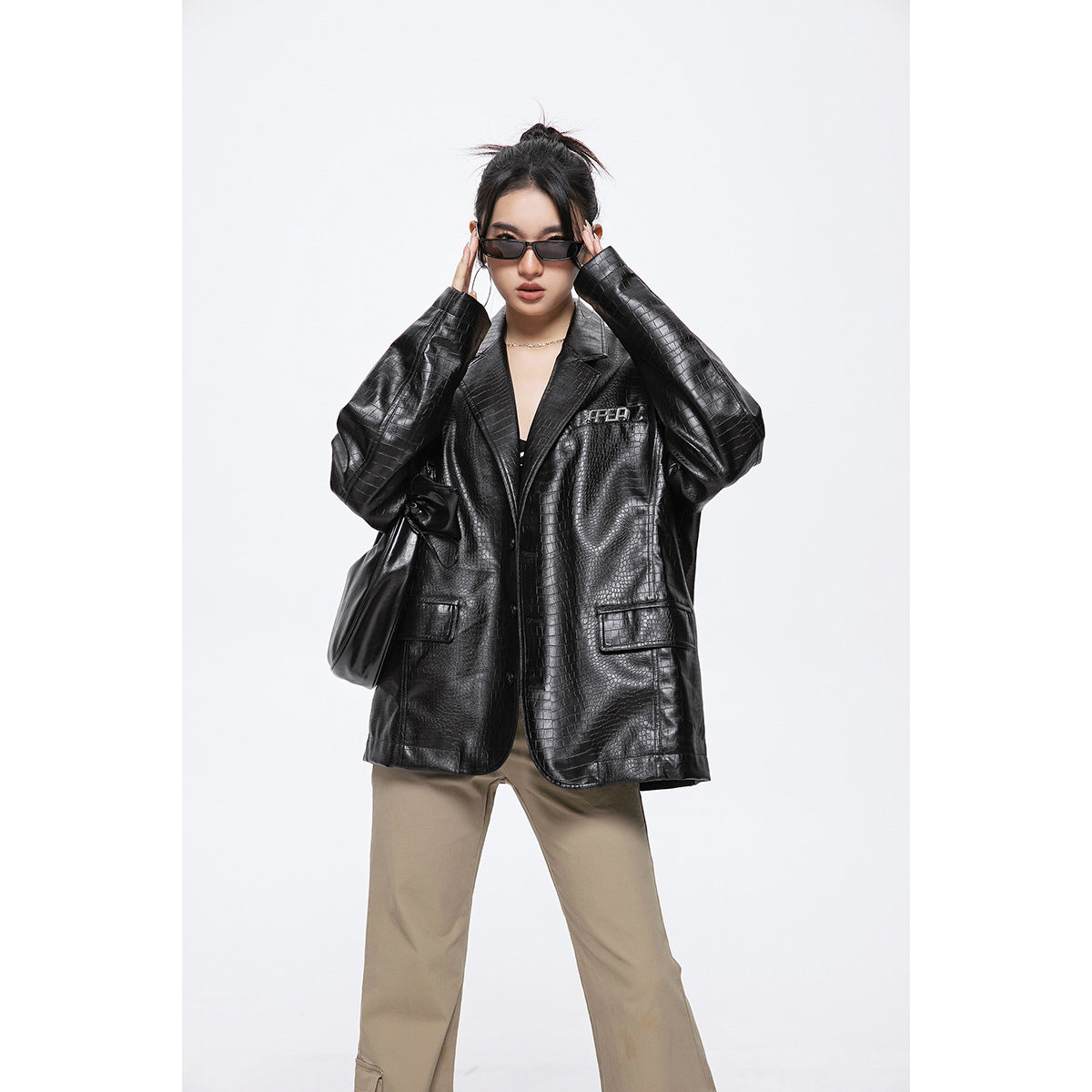 Model wearing an oversized black crocodile-embossed blazer with beige trousers, sunglasses and a shoulder bag.