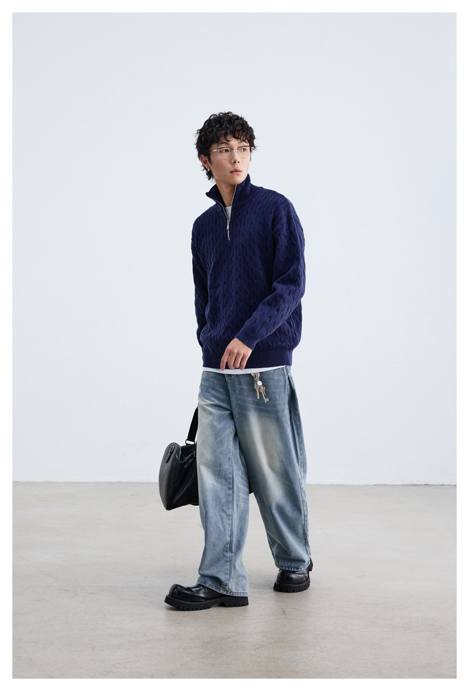 Model wearing a navy cable-knit quarter-zip sweater with wide-leg light-wash jeans and black shoes.