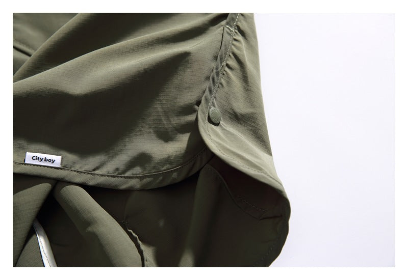 Close-up of olive-gray garment hem, a small button, stitching, and a sewn-in “City boy” label.