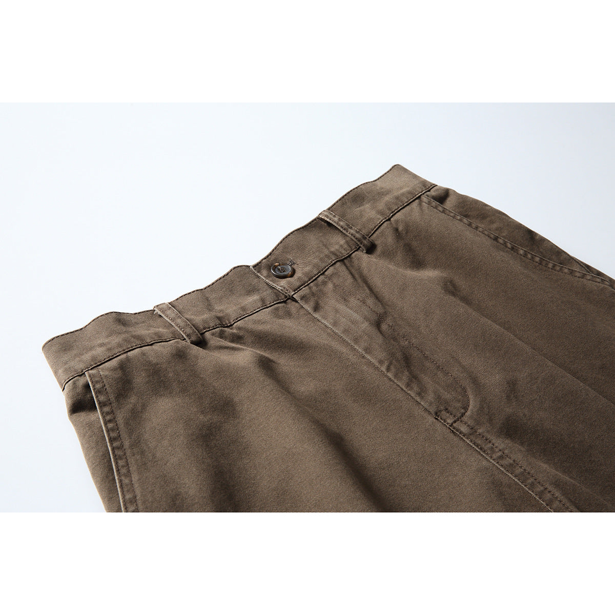 Close-up of brown trousers showing the waistband, button, belt loops and front fly.