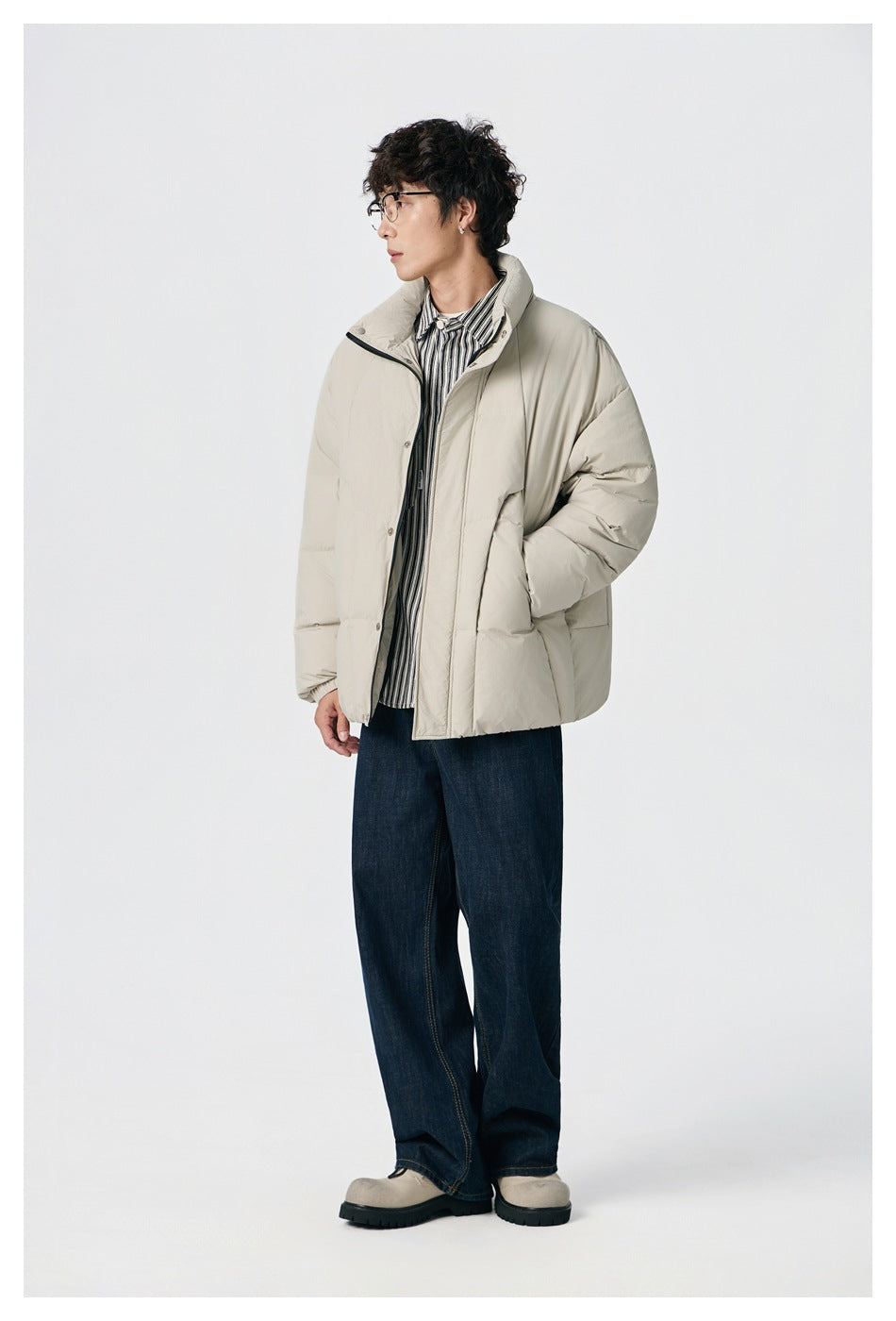 Side view of a model wearing a light beige padded jacket over a striped shirt and dark jeans.