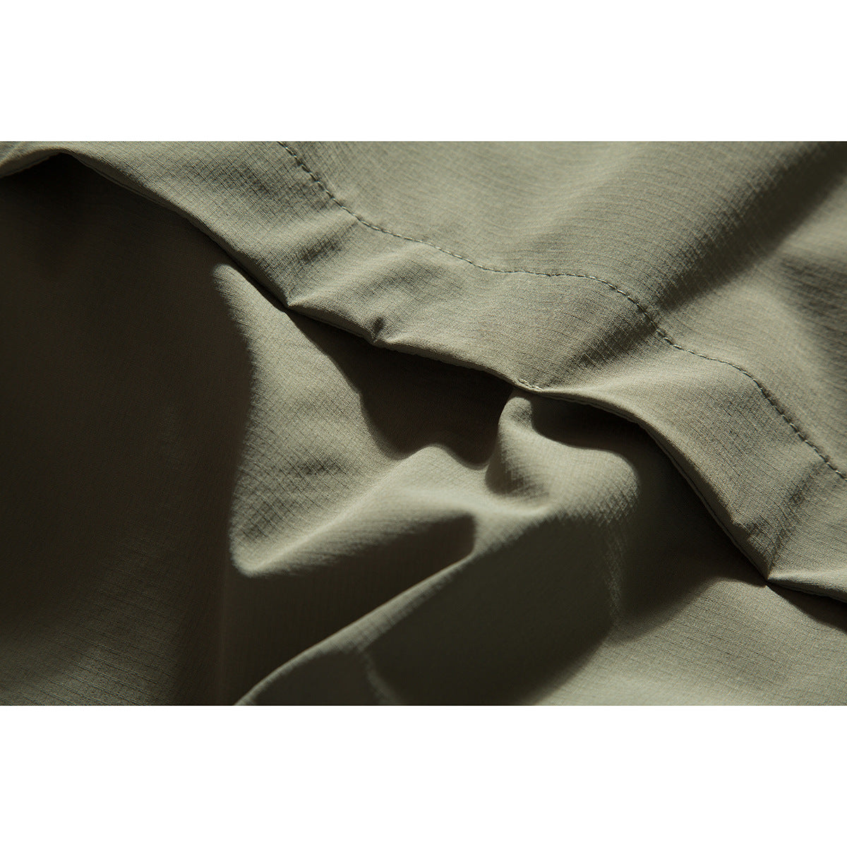 Close-up of olive-gray jacket fabric and a curved stitched seam.