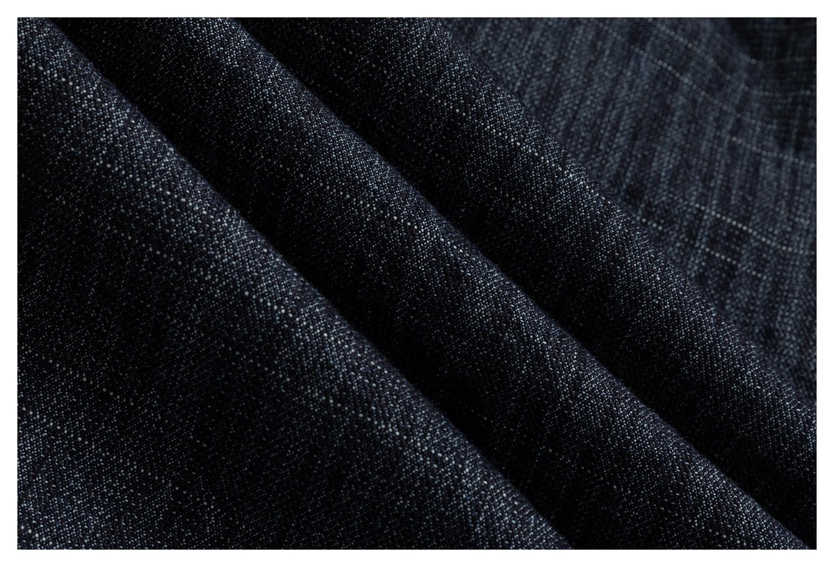 Macro close-up of dark indigo denim with visible woven texture and diagonal folds.