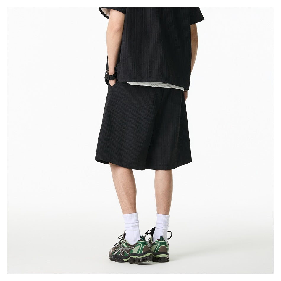 Back view of model wearing black textured wide-leg knee-length shorts with matching top, white socks and sneakers