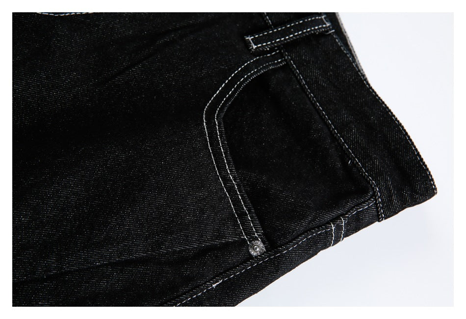 Close-up of black denim jeans showing a curved pocket, rivet, and white contrast stitching.