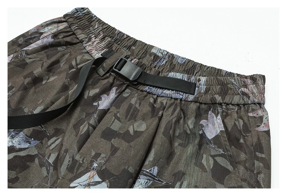 Angled close-up of camouflage-print pants showing the gathered waistband and black adjustable belt.