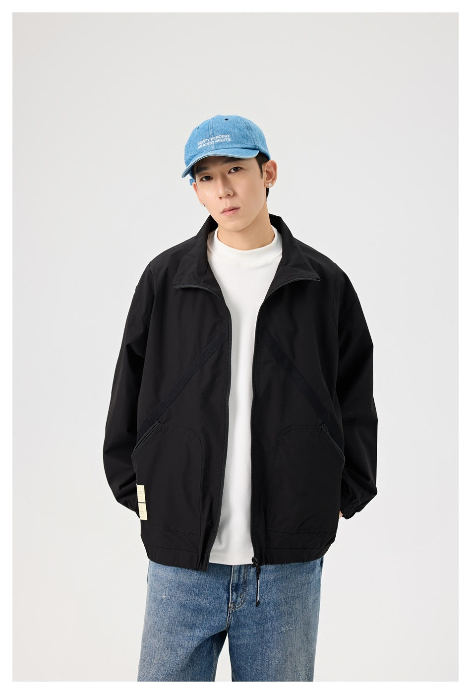 Model wearing open black stand-collar jacket with diagonal trim and zip pockets over white top and jeans