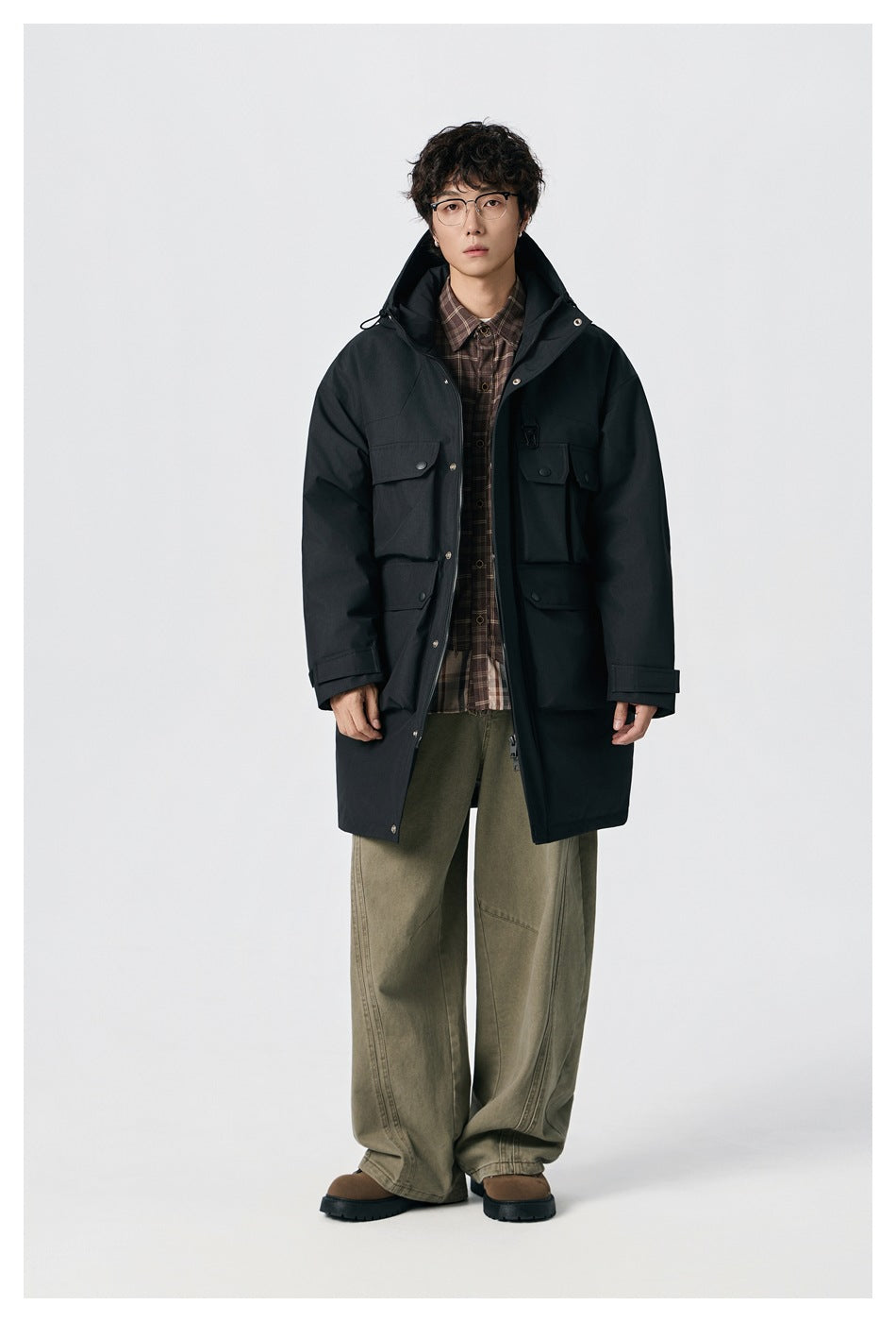 Front view of a model wearing a black hooded parka with multiple flap pockets.