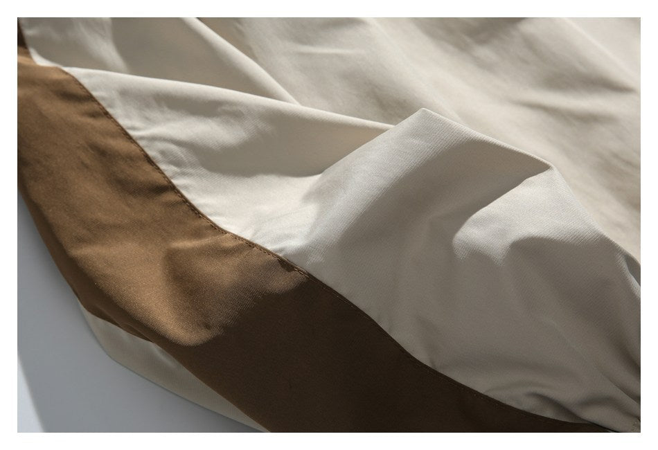 Close-up of cream fabric with a broad brown contrast panel and stitched seam.